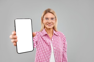 Happy woman holding smartphone with blank screen on grey background
