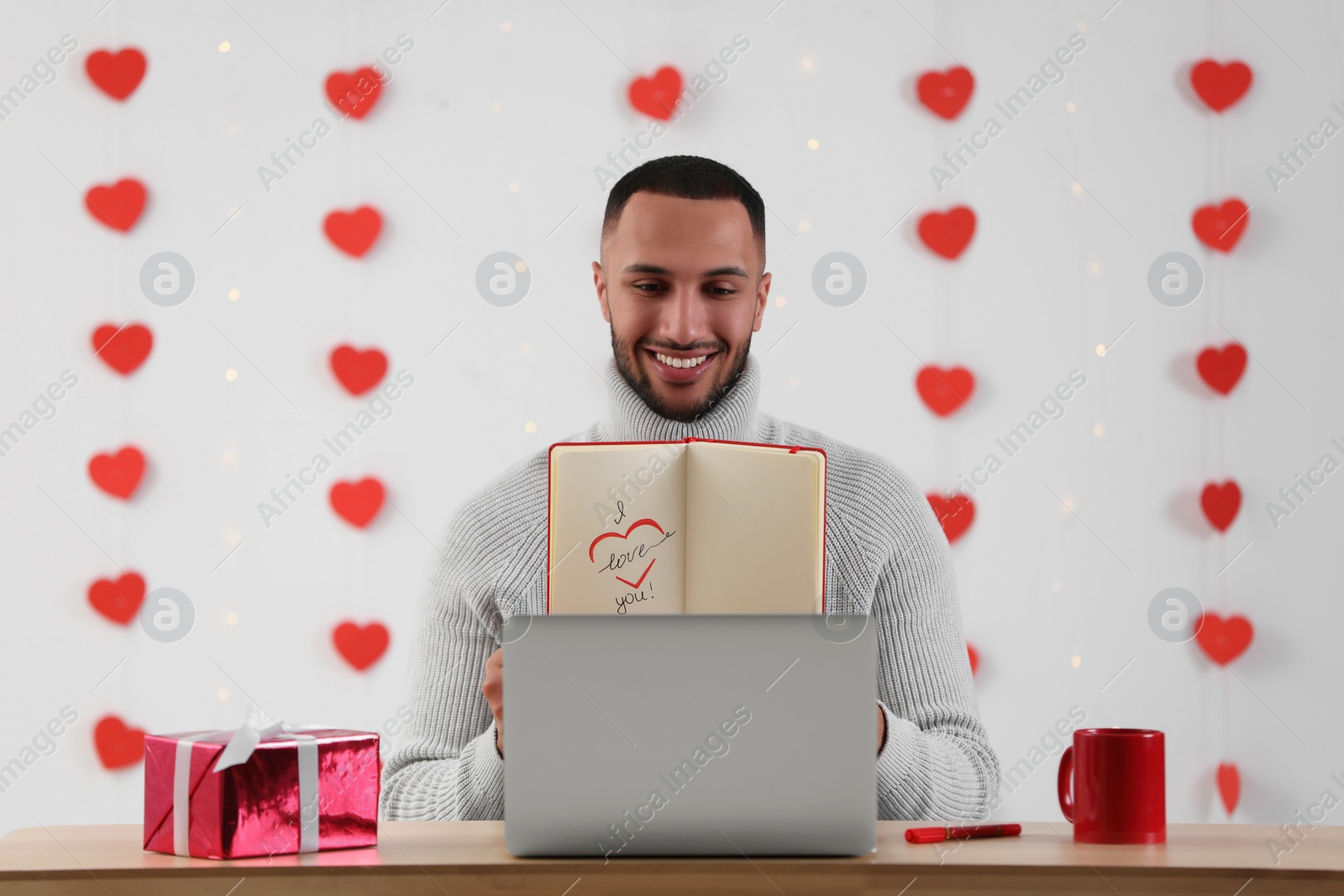 Photo of Valentine's day celebration in long distance relationship. Man having video chat with his girlfriend via laptop indoors