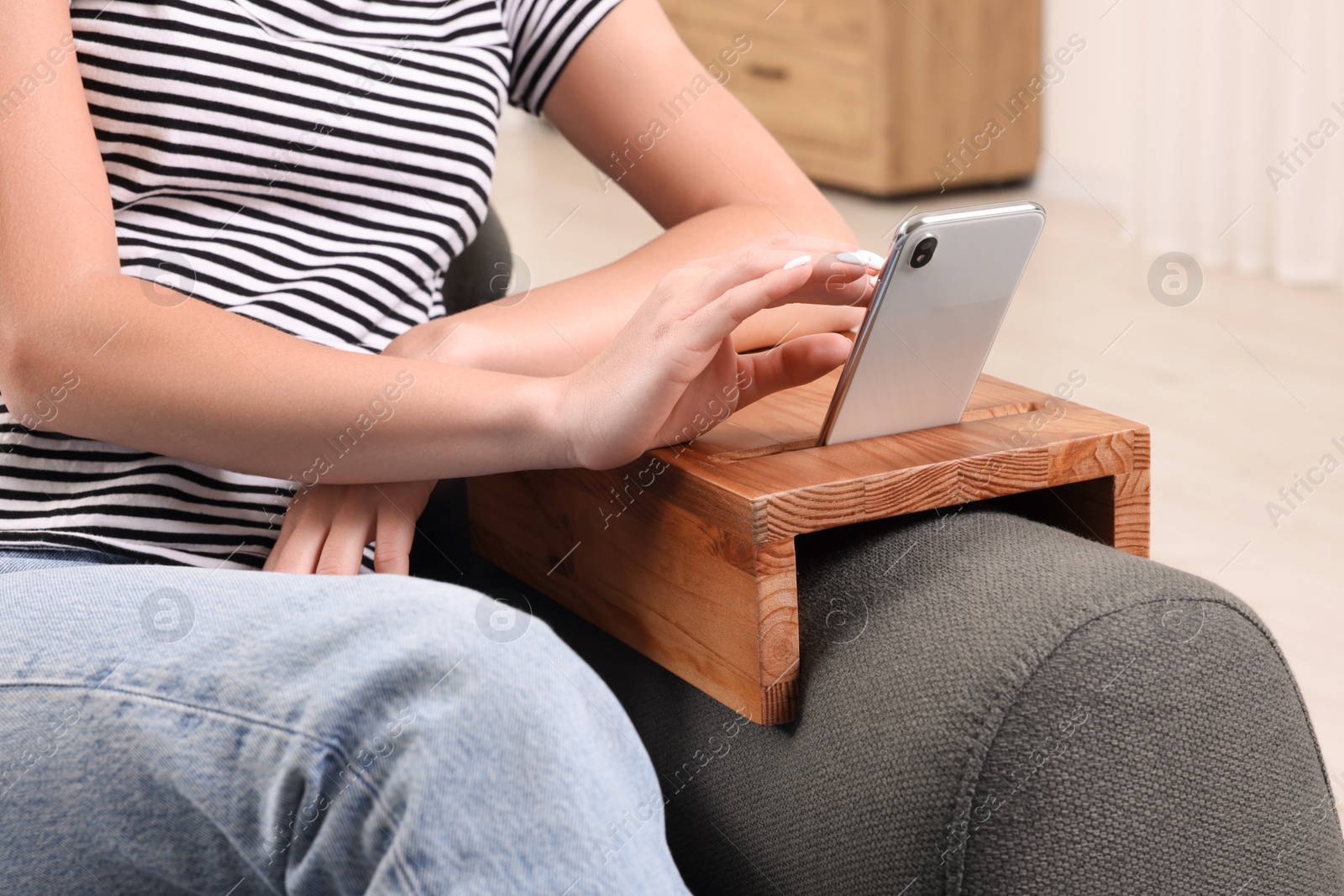 Photo of Woman using smartphone on sofa armrest wooden table at home, closeup