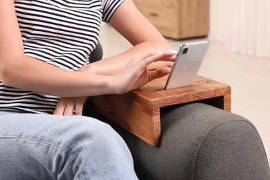 Woman using smartphone on sofa armrest wooden table at home, closeup