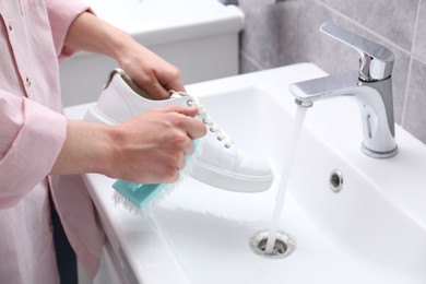 Photo of Woman washing stylish sneakers with brush in sink, closeup