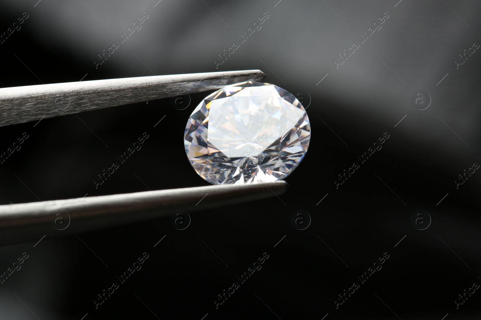 Photo of Tweezers with beautiful shiny diamond on dark background, closeup