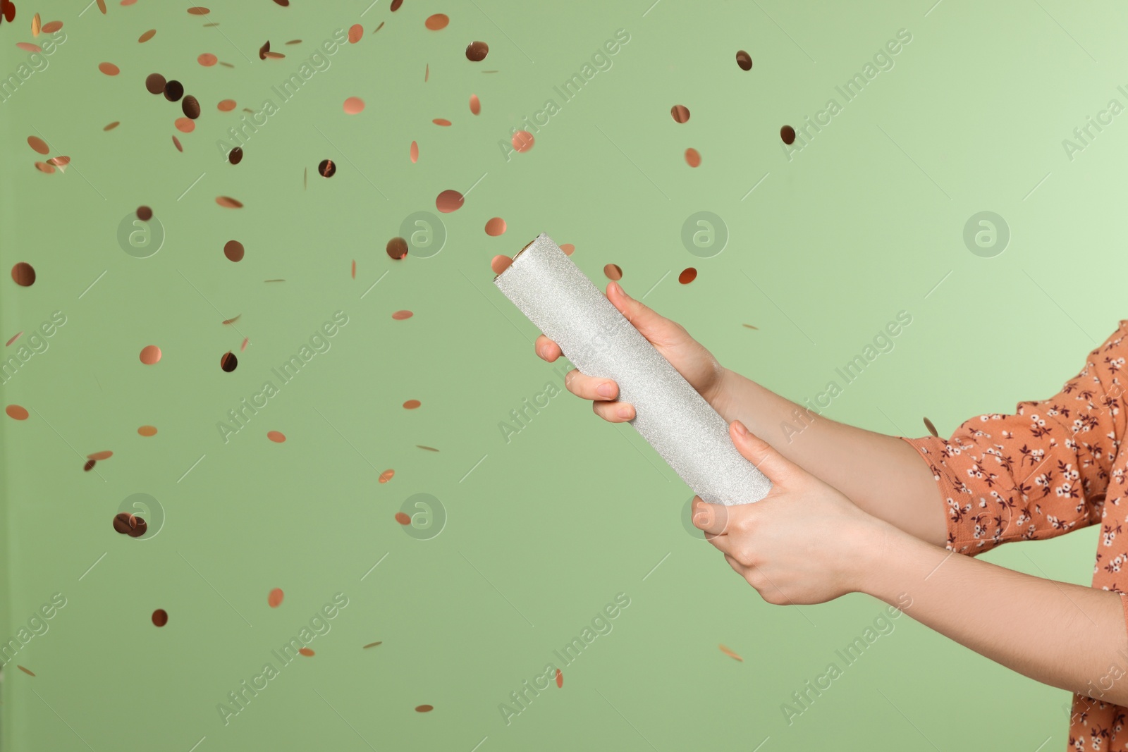 Photo of Young woman blowing up party popper on green background, closeup