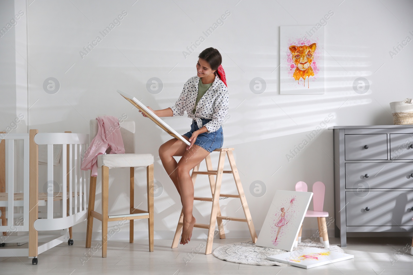 Photo of Decorator with picture on ladder in baby room. Interior design