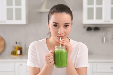 Photo of Beautiful young woman drinking delicious smoothie in kitchen