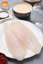 Different ingredients for soda water batter and raw fish fillet on grey table