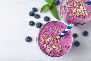 Glasses of tasty blueberry smoothie on white wooden table, flat lay