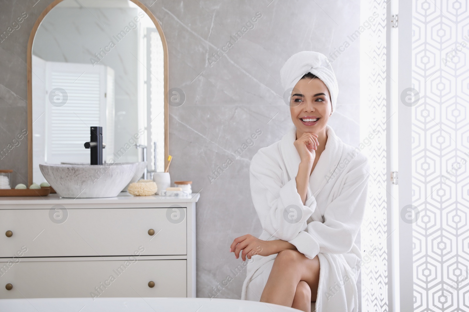 Photo of Beautiful young woman wearing soft white robe in bathroom