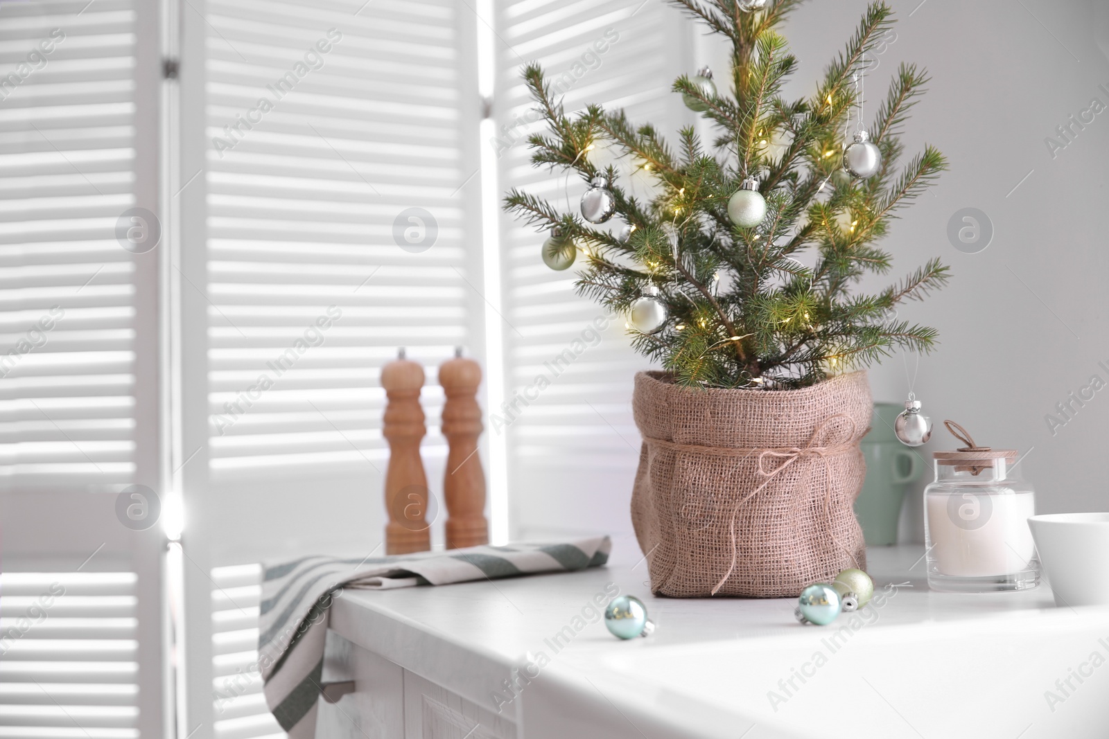 Photo of Small Christmas tree decorated with baubles and festive lights in kitchen