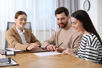 Couple signing document while having meeting with lawyer in office, selective focus