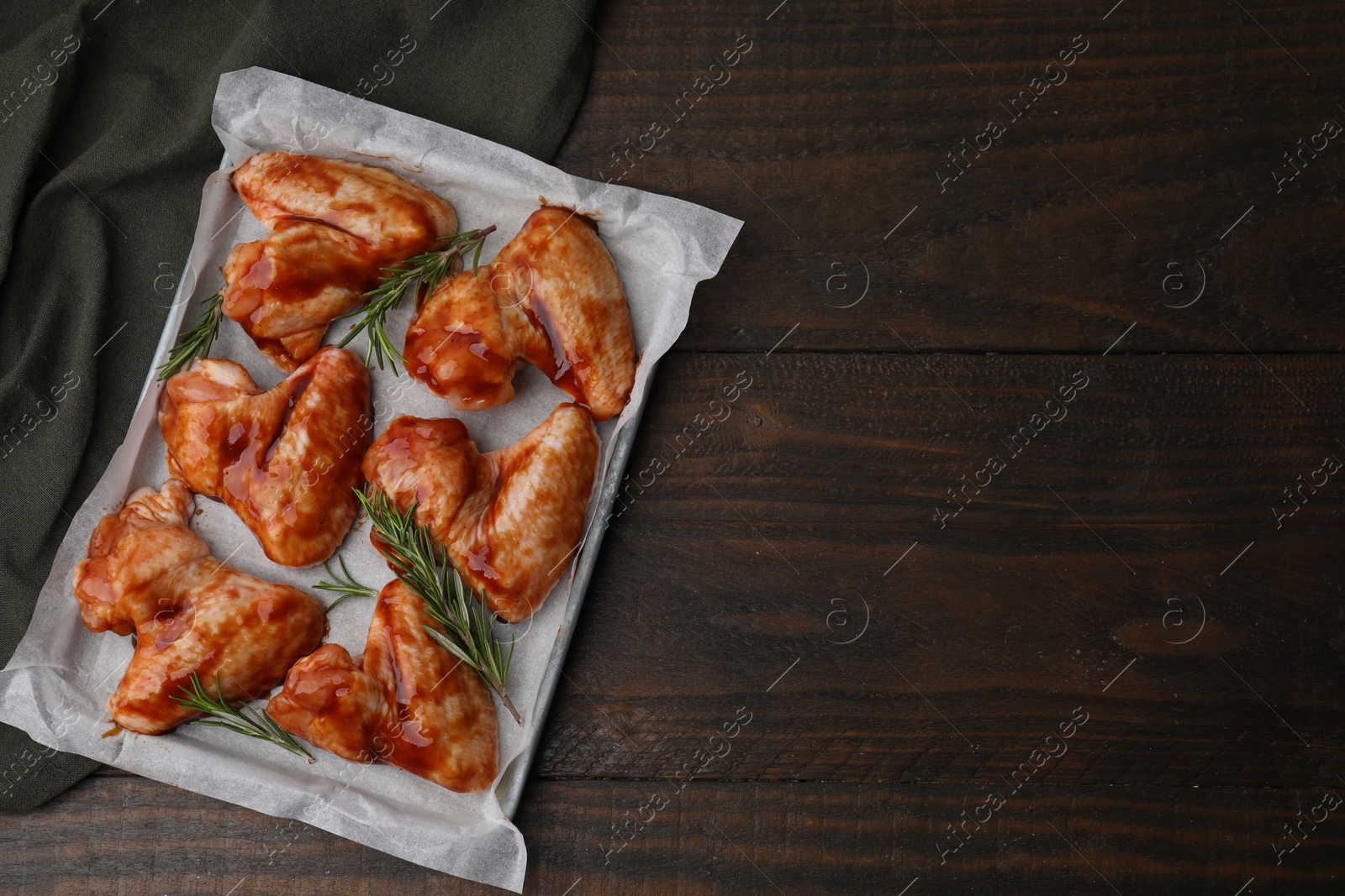 Photo of Raw marinated chicken wings and rosemary on wooden table, top view. Space for text