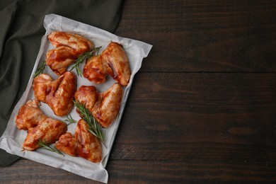 Photo of Raw marinated chicken wings and rosemary on wooden table, top view. Space for text