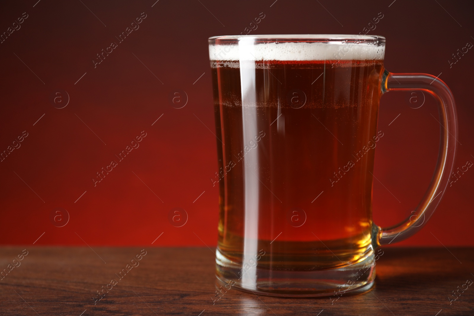 Photo of Mug with fresh beer on wooden table against color background, closeup. Space for text