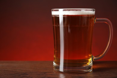 Mug with fresh beer on wooden table against color background, closeup. Space for text