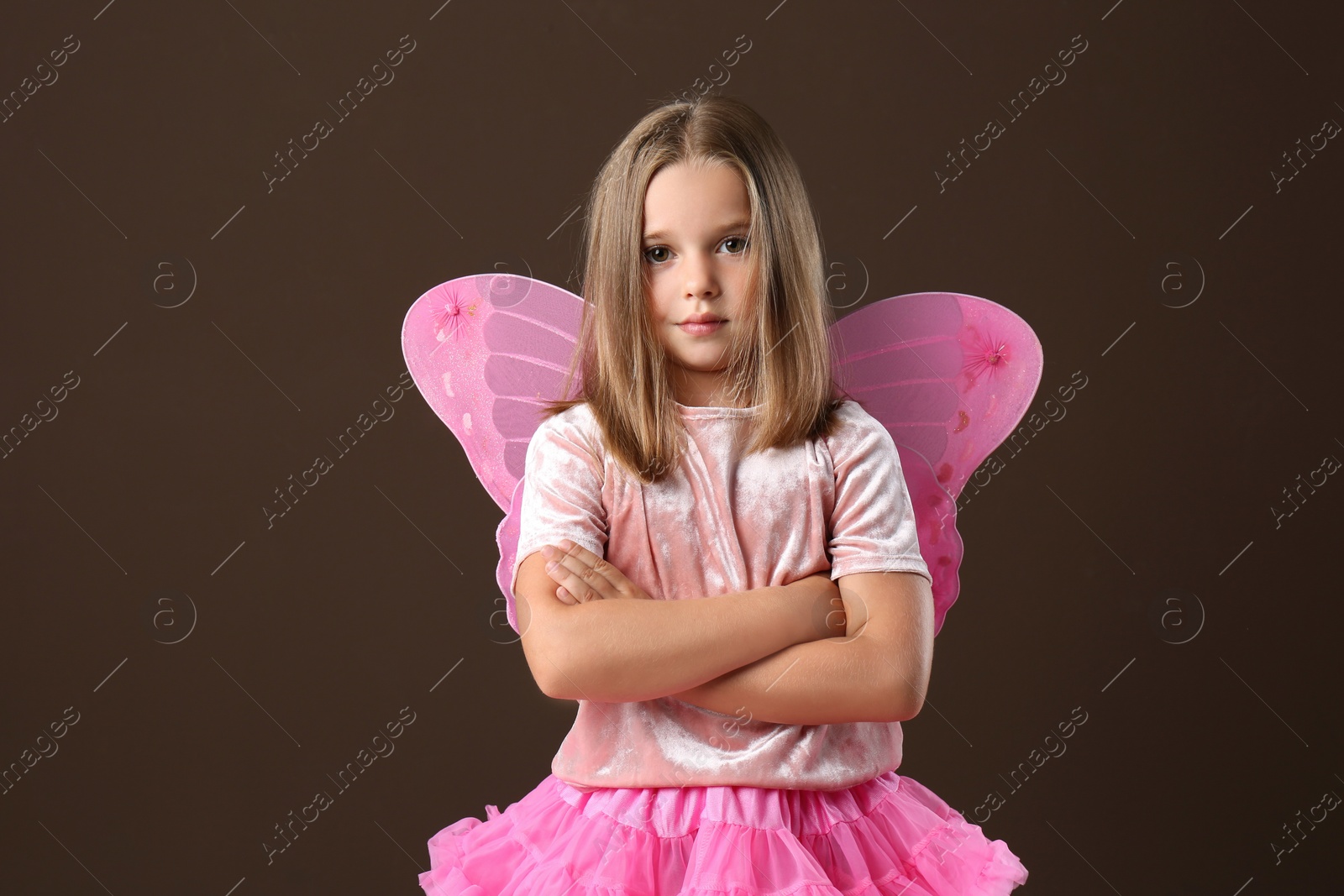 Photo of Cute little girl in fairy costume with pink wings on brown background