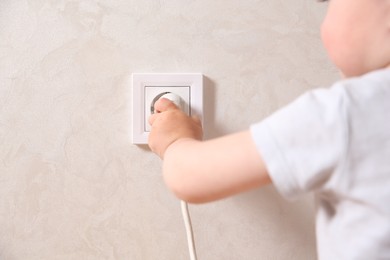 Little child playing with electrical socket and plug indoors, closeup. Dangerous situation