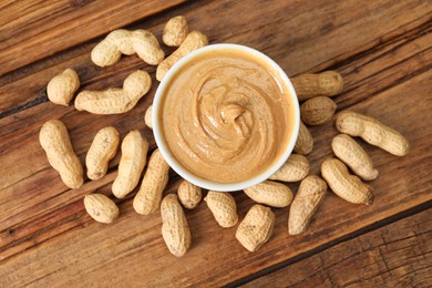 Photo of Delicious nut butter in bowl and peanuts on wooden table, top view