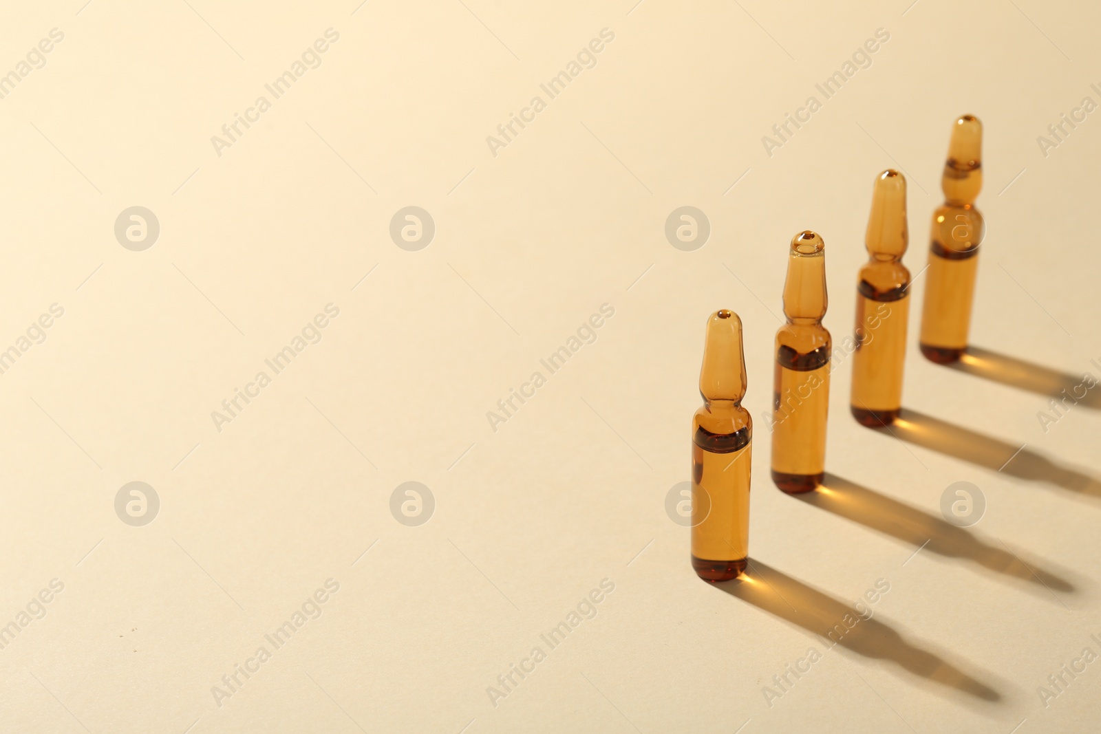 Photo of Glass ampoules with liquid on beige background. Space for text