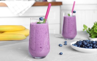 Photo of Glasses of delicious blueberry smoothie on light marble table in kitchen