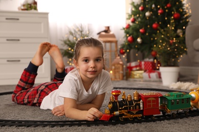 Photo of Little girl playing with colorful train toy in room decorated for Christmas