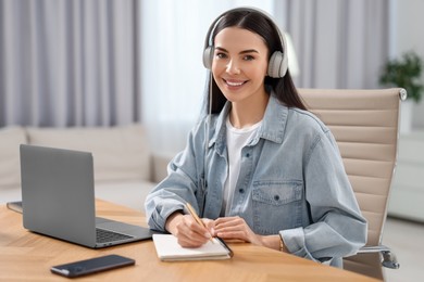 Young woman in headphones watching webinar at table in room