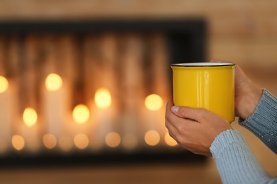 Woman with cup of hot drink near decorative fireplace indoors, closeup. Winter atmosphere