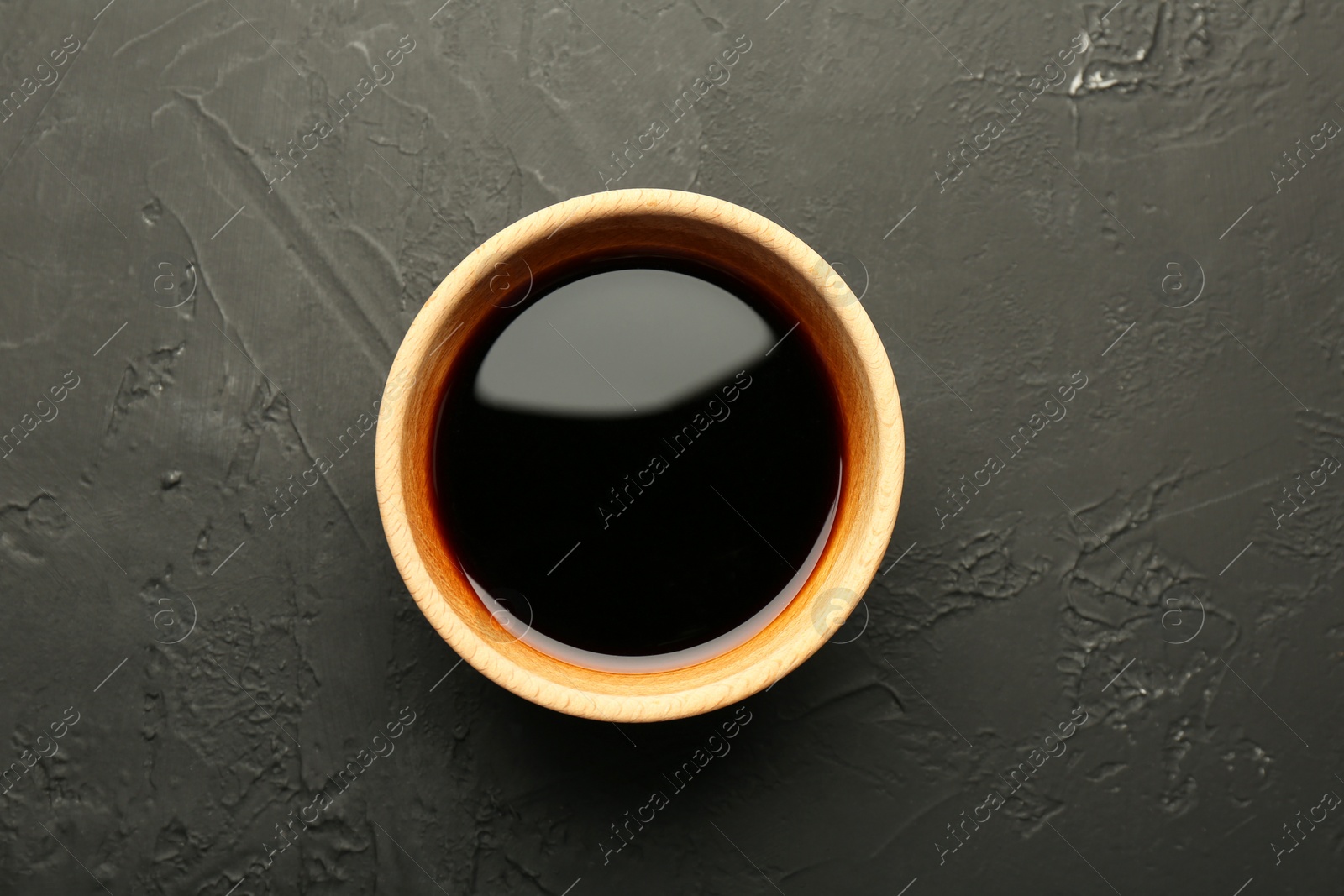 Photo of Soy sauce in wooden bowl on black textured table, top view