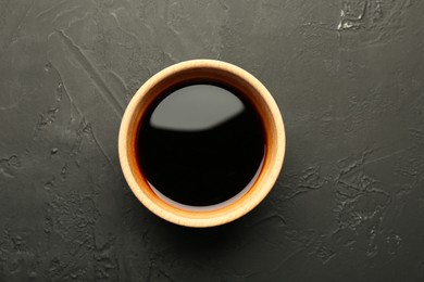 Soy sauce in wooden bowl on black textured table, top view