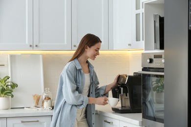 Photo of Young woman preparing fresh aromatic coffee with modern machine in kitchen