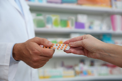 Image of Professional pharmacist giving pills to customer in drugstore, closeup