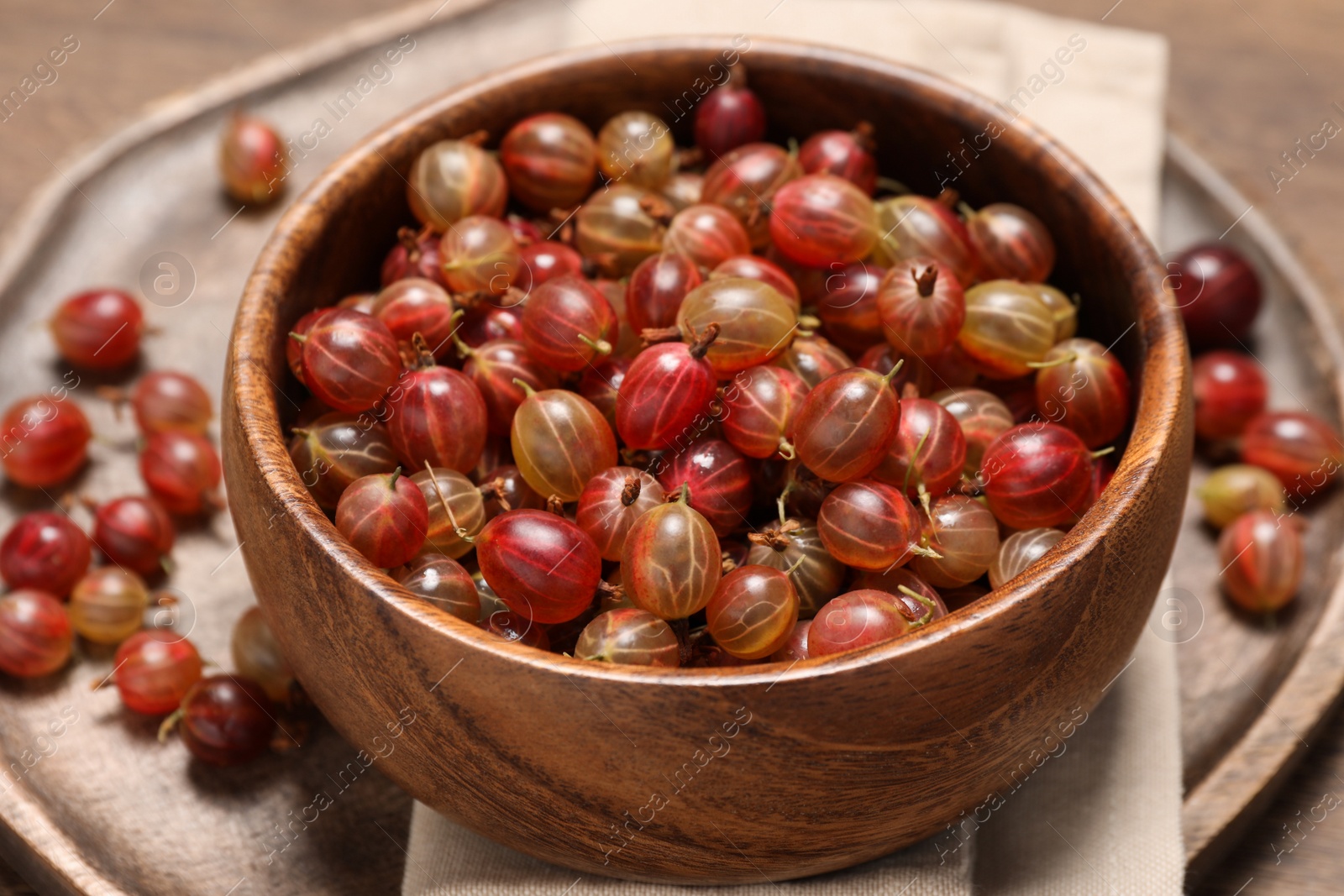 Photo of Bowl of fresh ripe gooseberries on wooden table, closeup