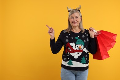 Photo of Happy senior woman in Christmas sweater and deer headband with shopping bags on orange background. Space for text
