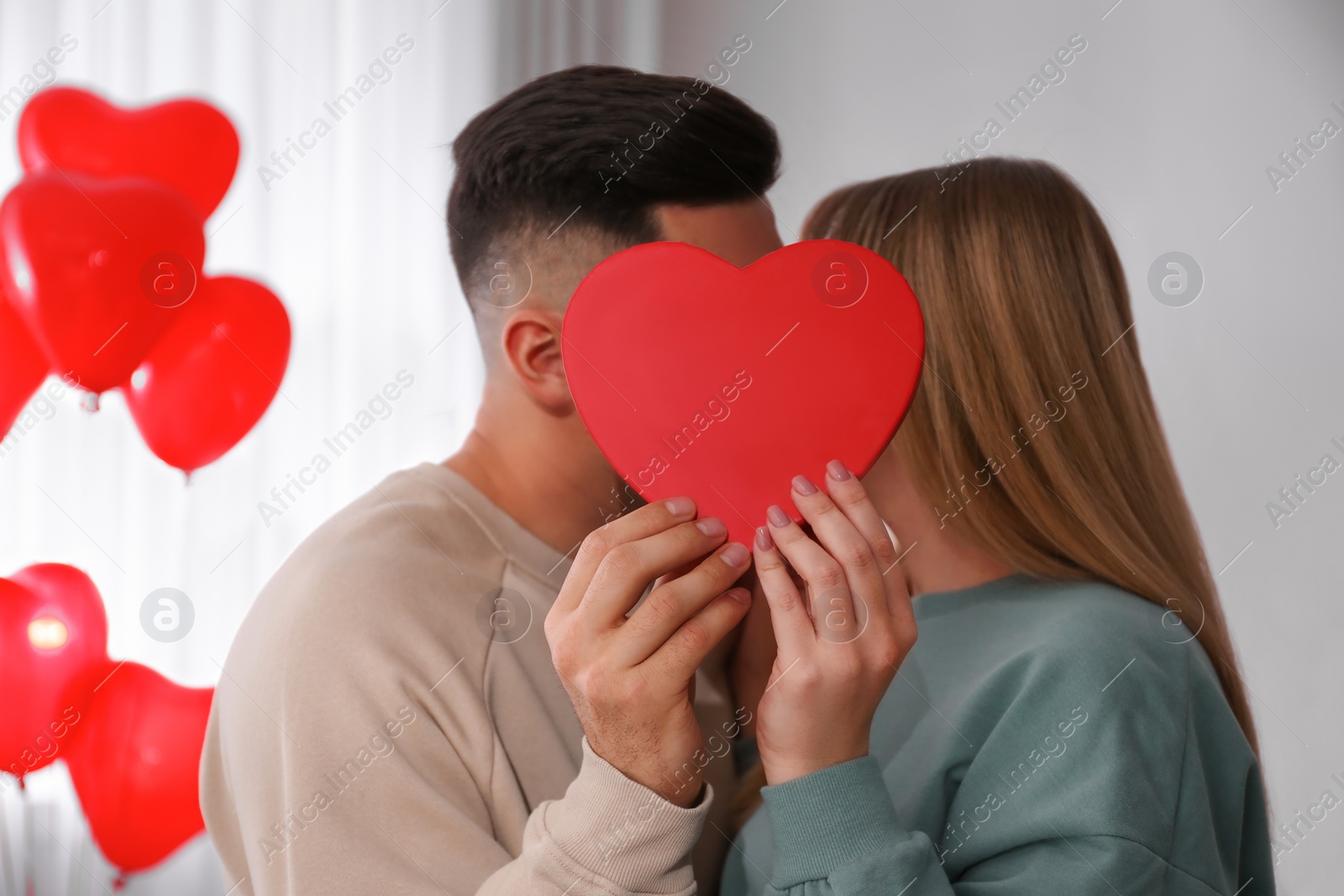 Photo of Lovely couple kissing behind decorative heart at home. Valentine's day celebration