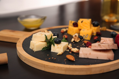 Different types of delicious cheeses, berries and nuts on table, closeup