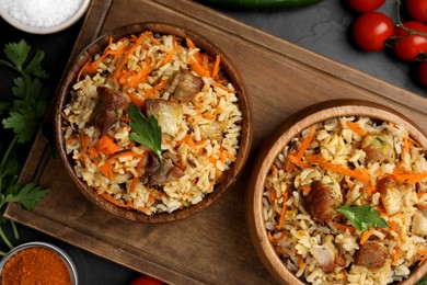 Photo of Delicious pilaf in bowls and products on black table, flat lay