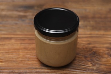 Tasty nut paste in jar on wooden table, closeup