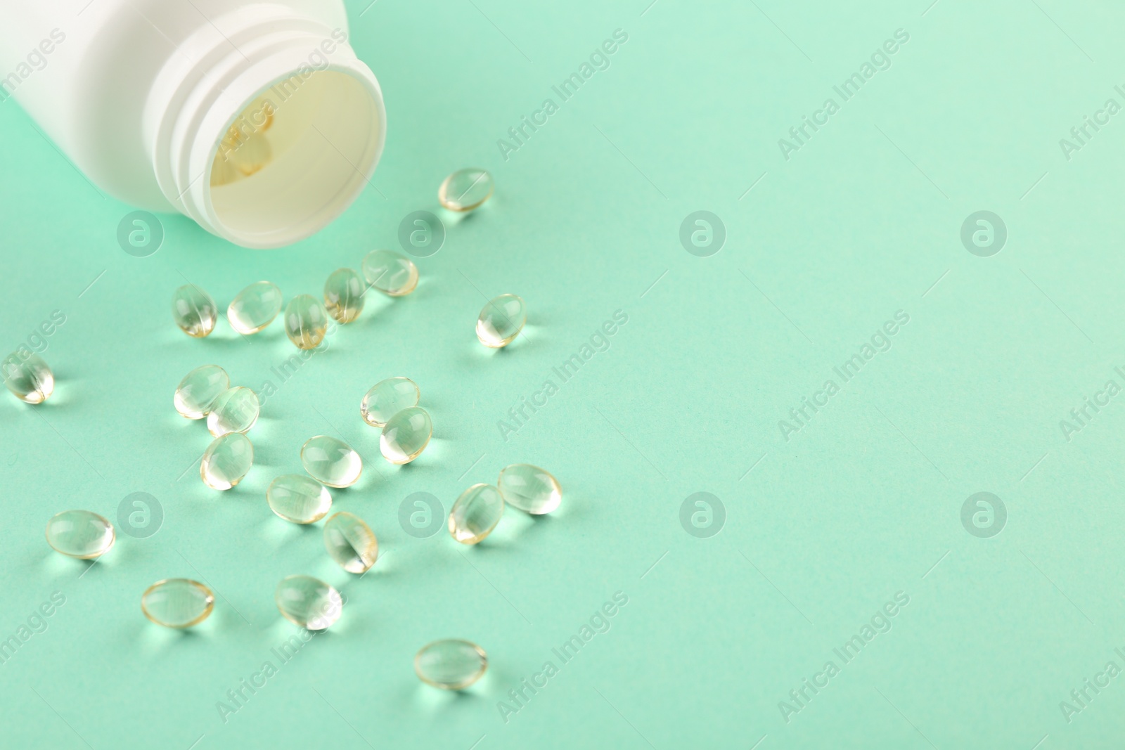 Photo of Bottle and vitamin capsules on turquoise background, closeup. Space for text