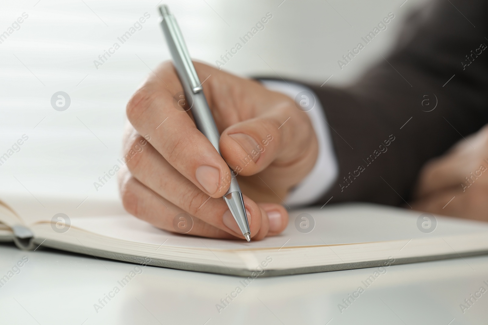 Photo of Man writing in notebook at white table, closeup