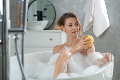 Beautiful woman with sponge taking bath indoors