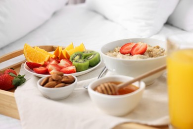 Photo of Tasty breakfast served in bed. Oatmeal, juice, fruits, almonds and honey on tray, closeup