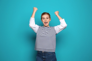 Happy young woman celebrating victory on color background