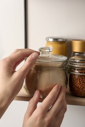 Photo of Woman taking glass jar of buckwheat flour from shelf, closeup