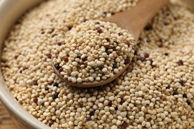 Photo of Raw quinoa seeds and spoon in bowl on table, closeup