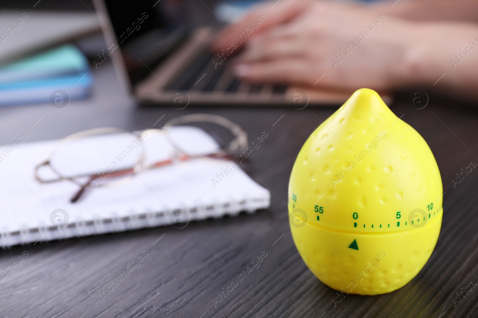 Photo of Woman working on laptop at wooden table, focus on kitchen timer in shape of lemon. Space for text