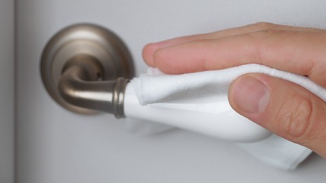 Man cleaning doorknob with wet wipe indoors, closeup. Protective measures