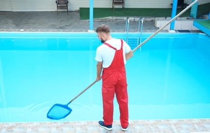 Photo of Male worker cleaning outdoor pool with scoop net