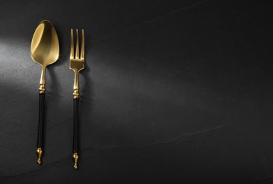 Photo of Shiny fork and spoon on black table, flat lay. Space for text