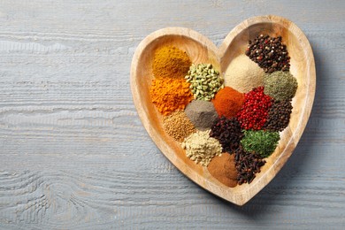 Photo of Heart shaped plate with different spices on grey wooden table, top view. Space for text