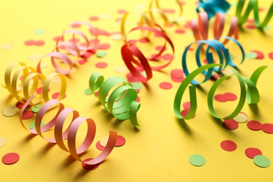 Colorful serpentine streamers and confetti on yellow background