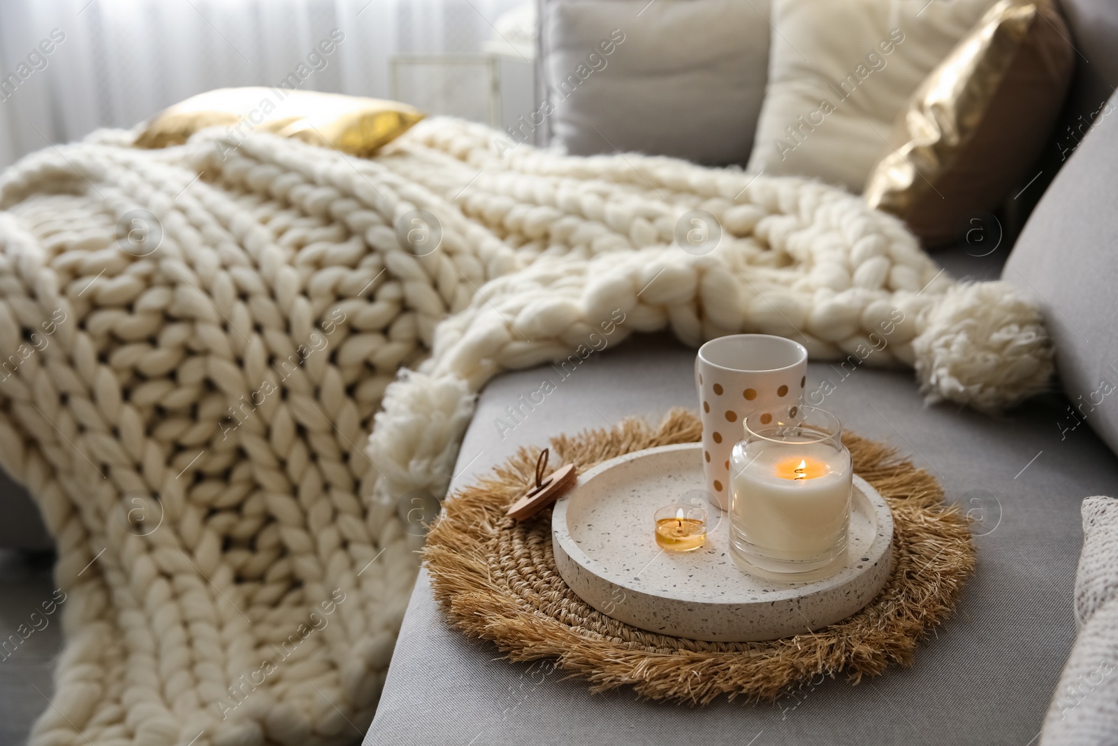 Photo of Cup of drink and burning candles on sofa in room, space for text. Interior elements